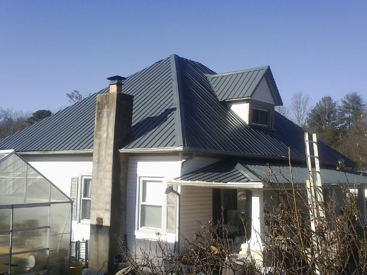 Dark blue standing seam metal roof on a white farmhouse with dormer — Slate & Tile Roof Repair by Roofing Brothers in Groves