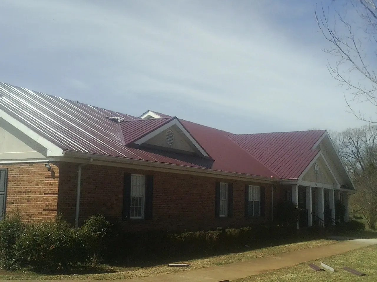 Red metal roof with gabled entries on a long brick building, from a Hail Damage Roof Repair job in Groves