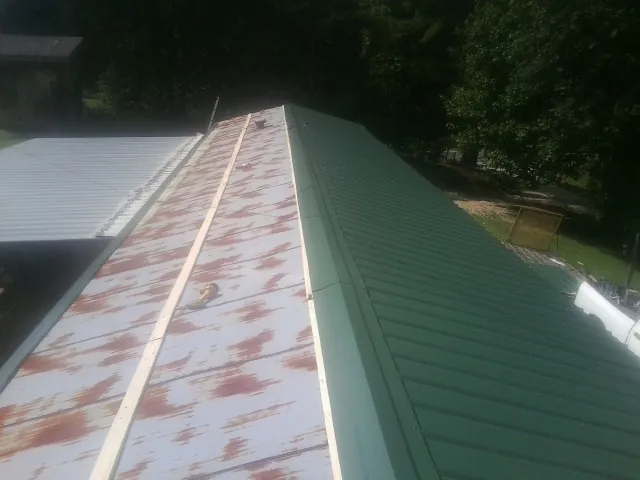 Old rusted panels beside newly installed green metal roofing — Wind Damage Roof Repair by Roofing Brothers in Groves