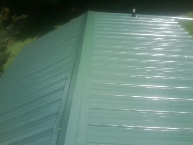 New green metal panels meeting at the ridge of a roof — Flat Roof Repair work by our crew in Groves