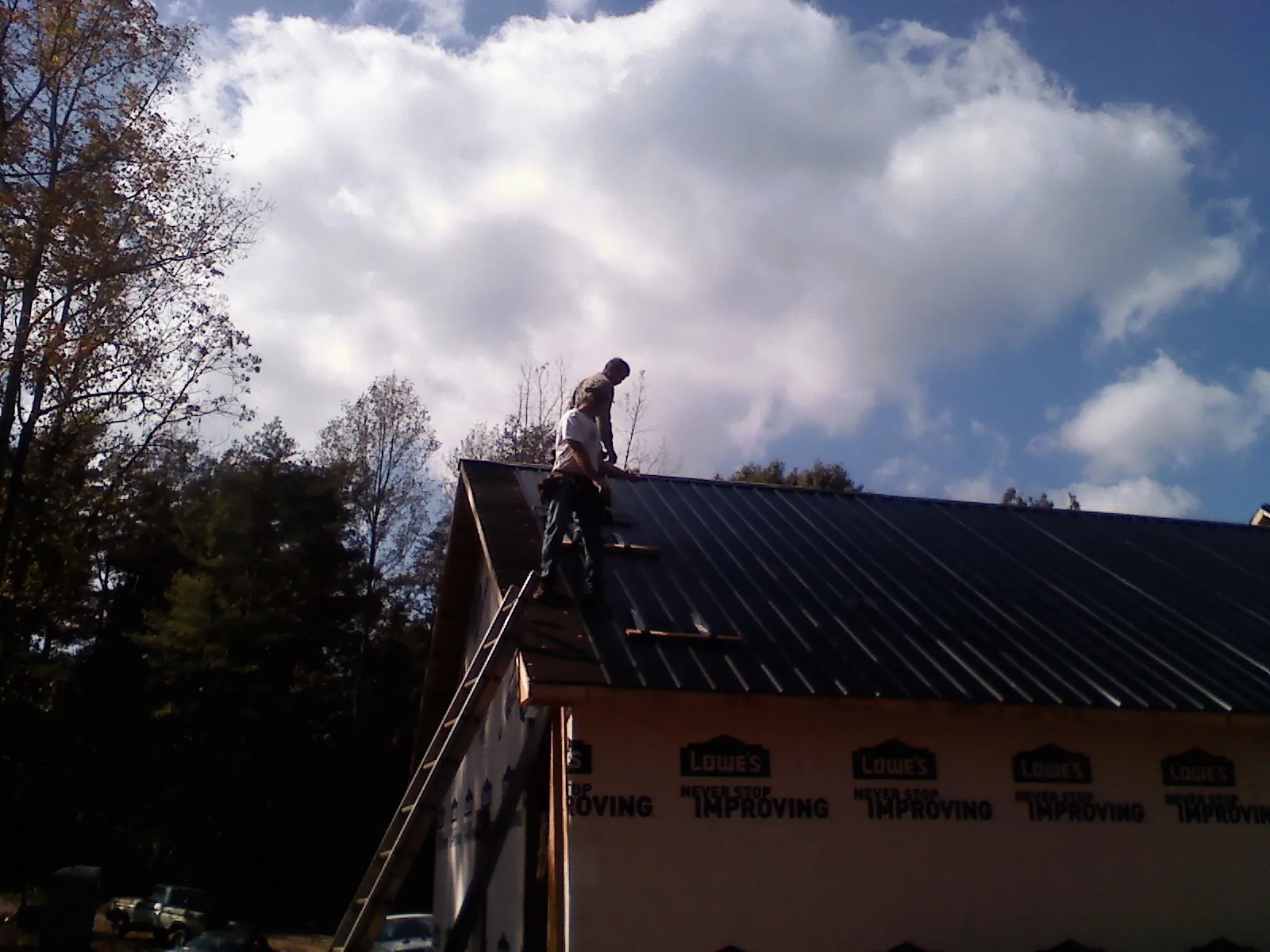 Roofer fastening dark metal panels high against a cloudy sky, from a Roof Inspection job in Groves